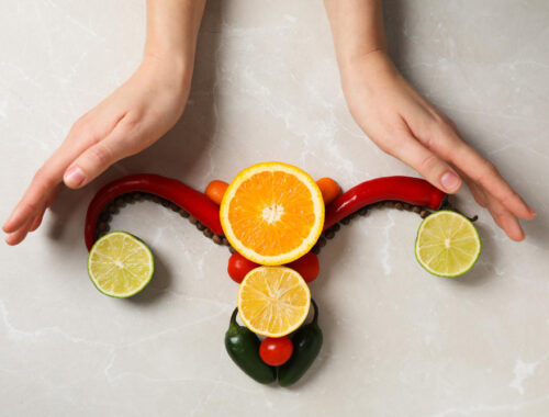 Manos rodeando una representación artística del útero hecha con frutas y verduras, simbolizando la sanación femenina.