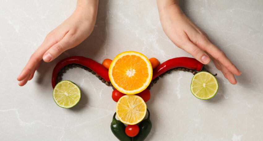Manos rodeando una representación artística del útero hecha con frutas y verduras, simbolizando la sanación femenina.