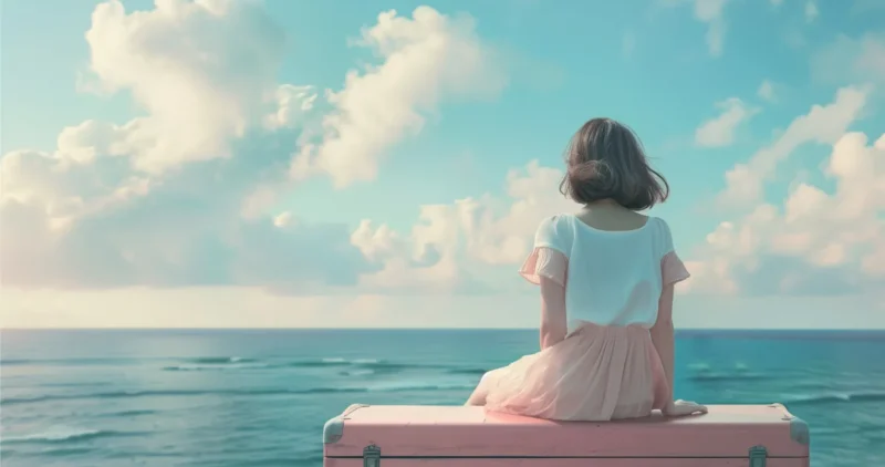 Una persona sentada sobre una maleta rosa, mirando el mar y el cielo despejado, evocando tranquilidad y reflexión.