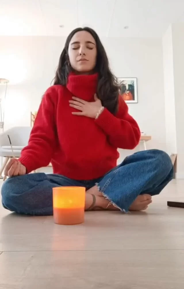 Mujer meditando en un ambiente tranquilo, con una vela encendida frente a ella, transmitiendo paz y concentración.